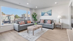 Uma sala de estar moderna com dois sofás cinza, uma mesa de centro de madeira e uma janela grande com vista para a cidade.