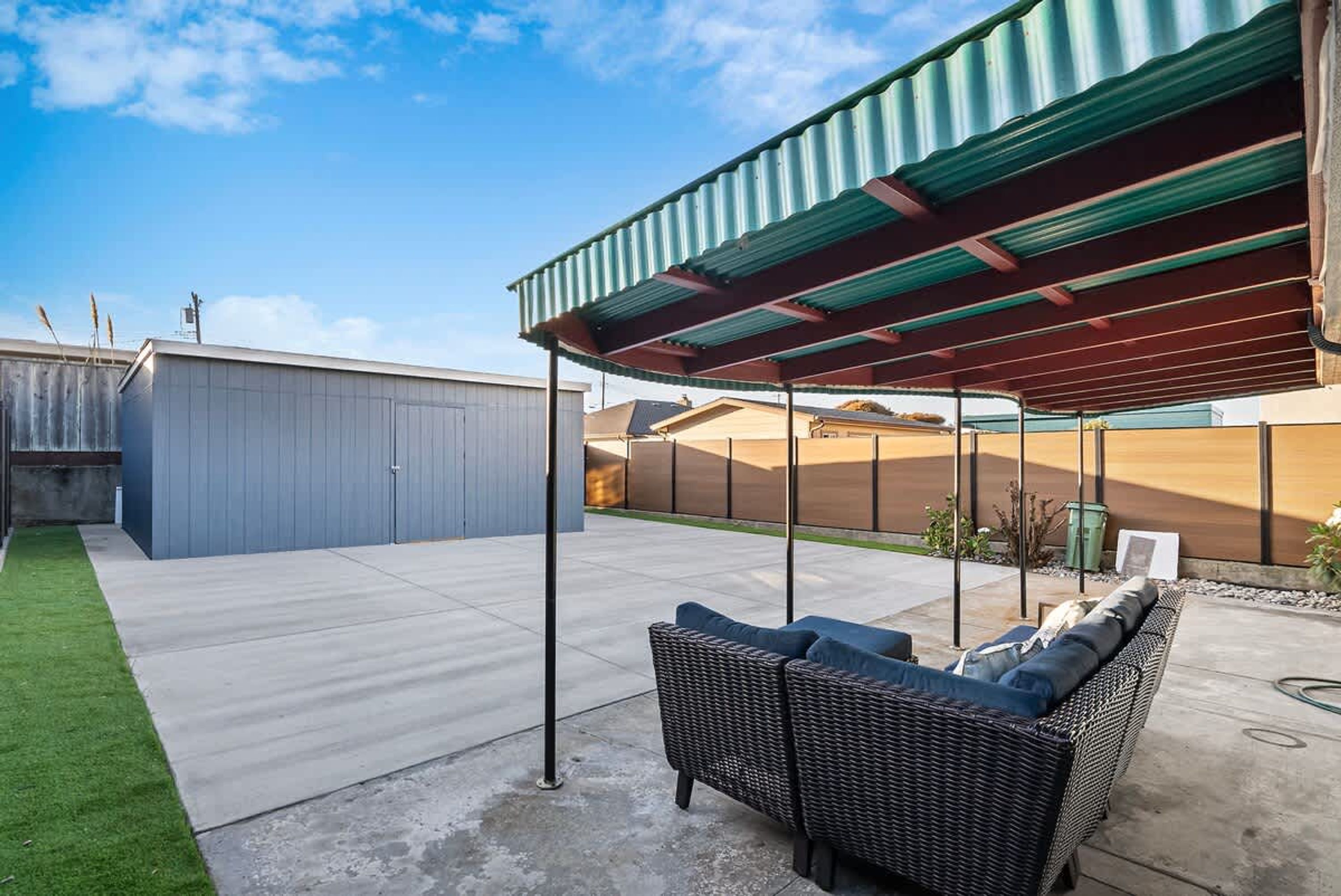 A covered patio area with a wicker sofa and a concrete floor.