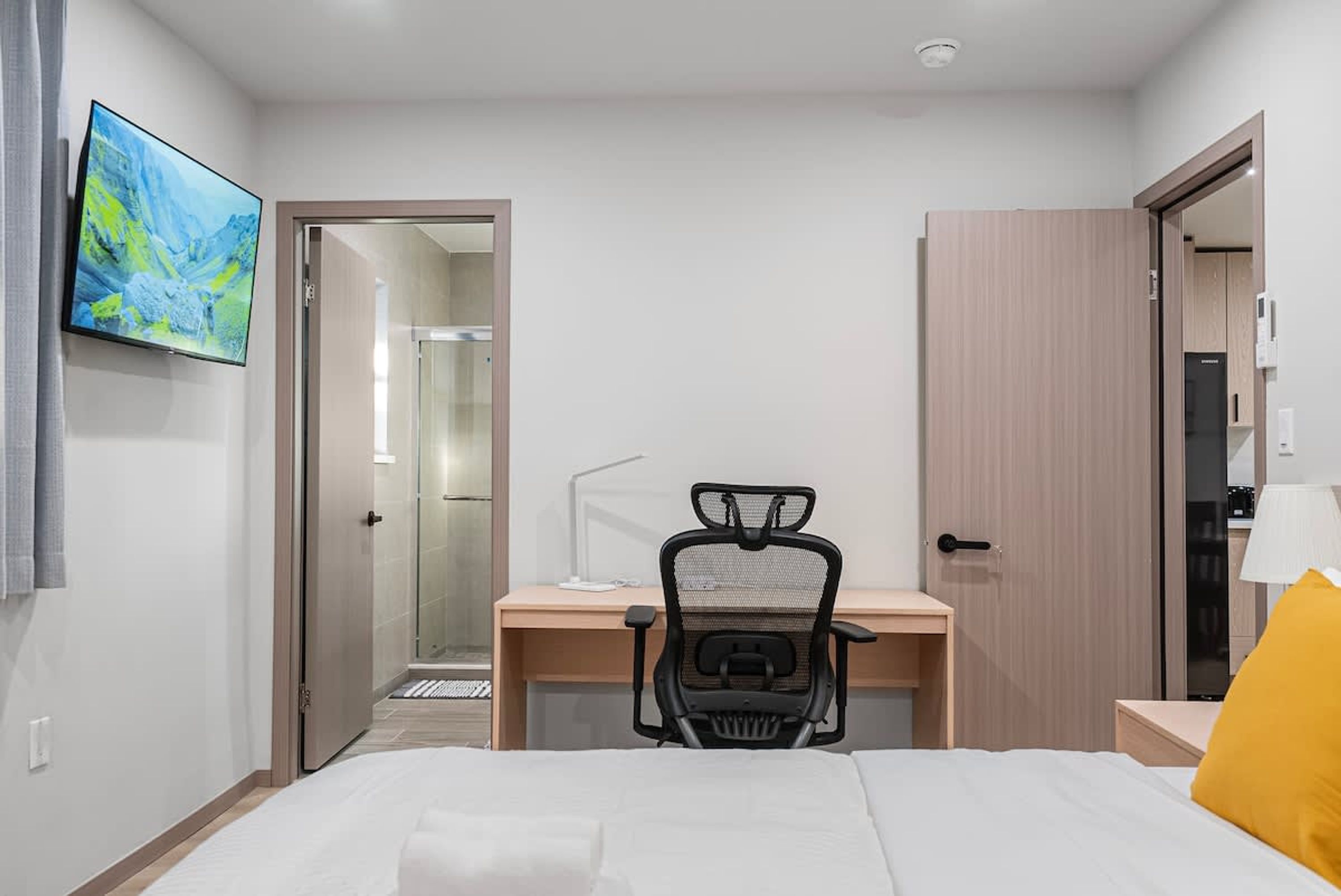 Une chambre d’hôtel avec un lit, un bureau, une chaise, une télévision et une porte de salle de bain.