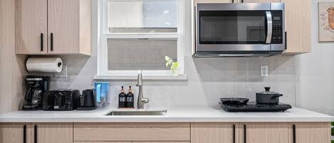A modern kitchen with wooden cabinets, a stainless steel microwave, a coffee maker, and a window with a view.