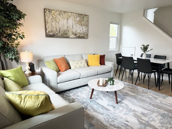 Un salon moderne avec un canapé gris, une table basse ronde et un coin repas comprenant des chaises noires et une table blanche.