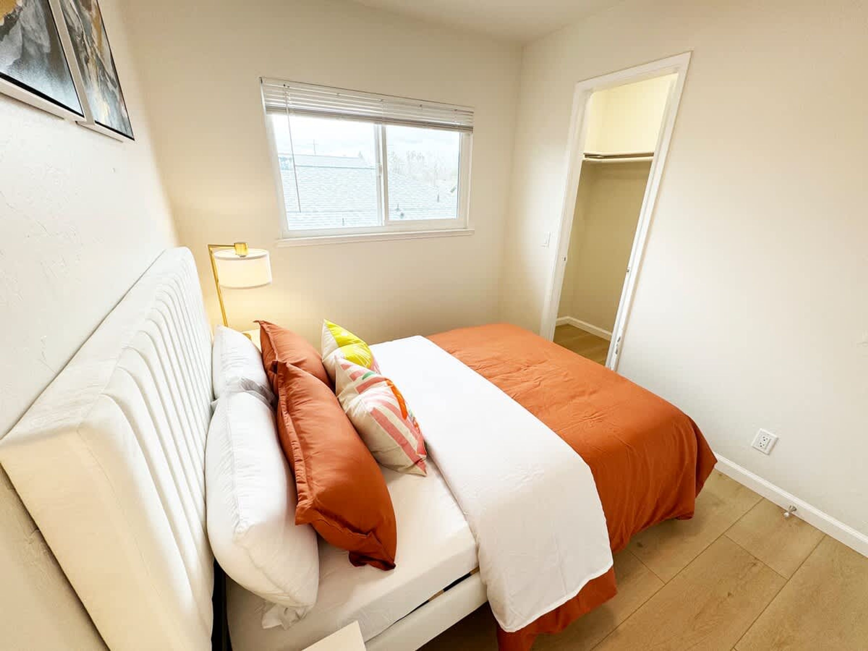 Ein Schlafzimmer mit Bett, Kissen, einer Nachttischlampe, einem Fenster und einer Tür.