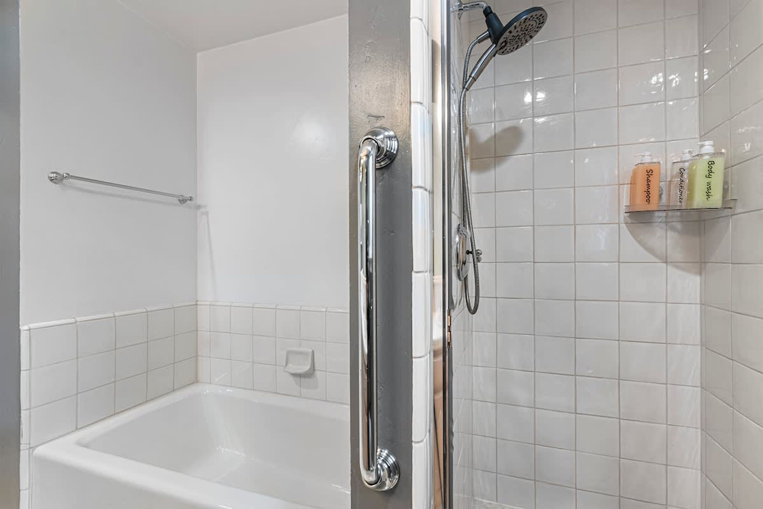 A shower area with a handheld showerhead, a glass-enclosed bathtub, and a shelf with toiletries.