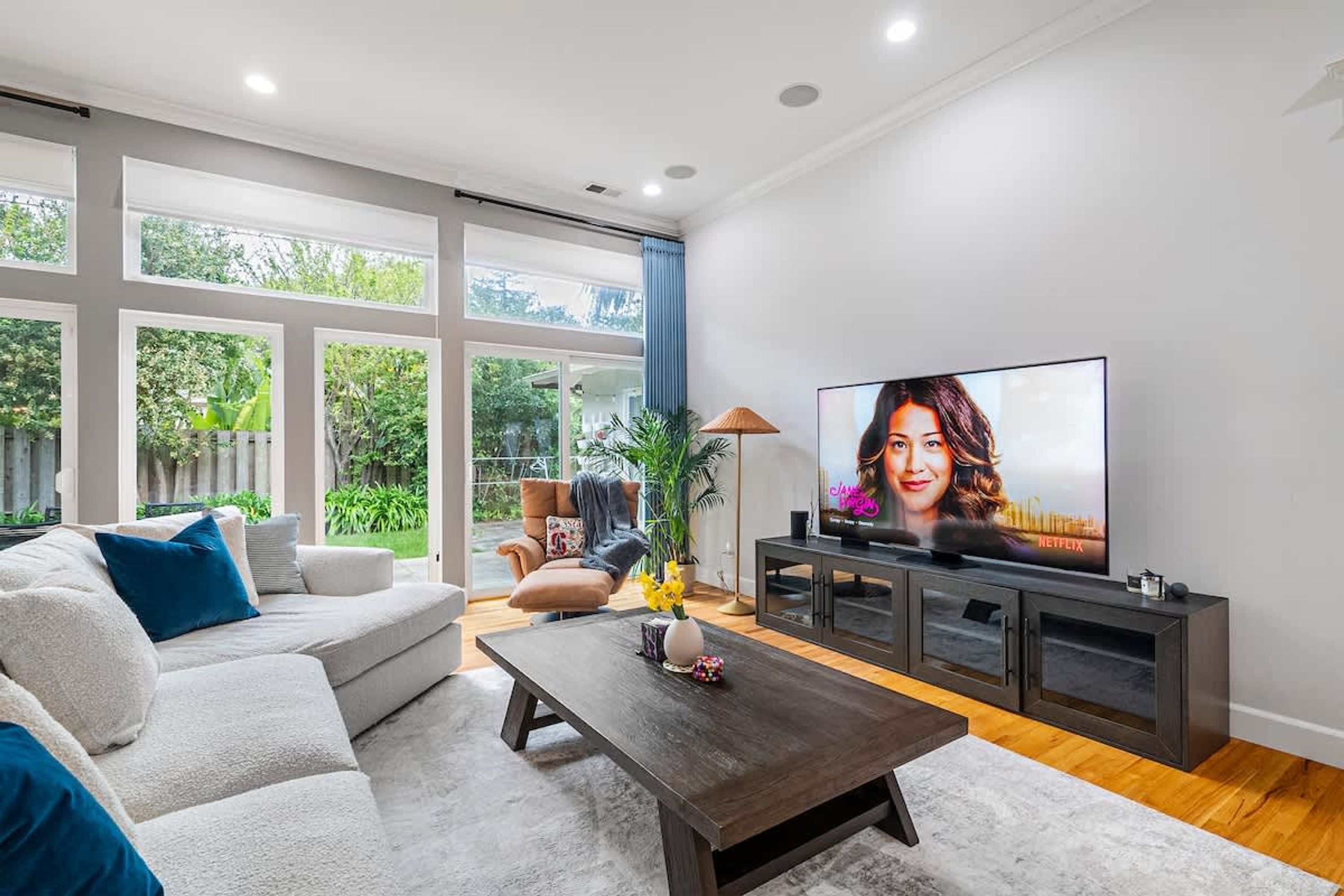 A modern living room with a large TV, a sofa, a coffee table, and a view of greenery outside.