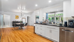 A modern kitchen with white cabinetry, a stainless steel dishwasher, and a large window providing natural light.