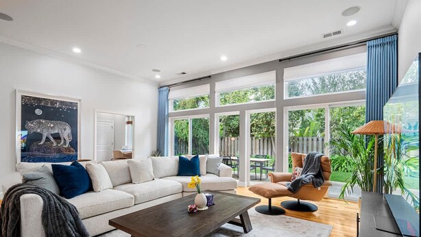 A modern living room with a sectional sofa, a coffee table, and a chair. There is a large window with a view of greenery outside.
