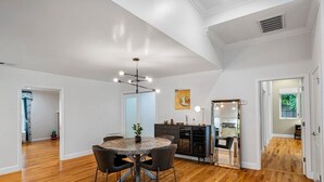 A spacious dining area with a round table and chairs, a modern chandelier, and a view into the kitchen.