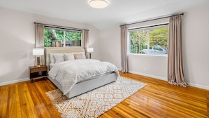 A bedroom with a bed, nightstands, a lamp, a window with curtains, and a view of the outside.
