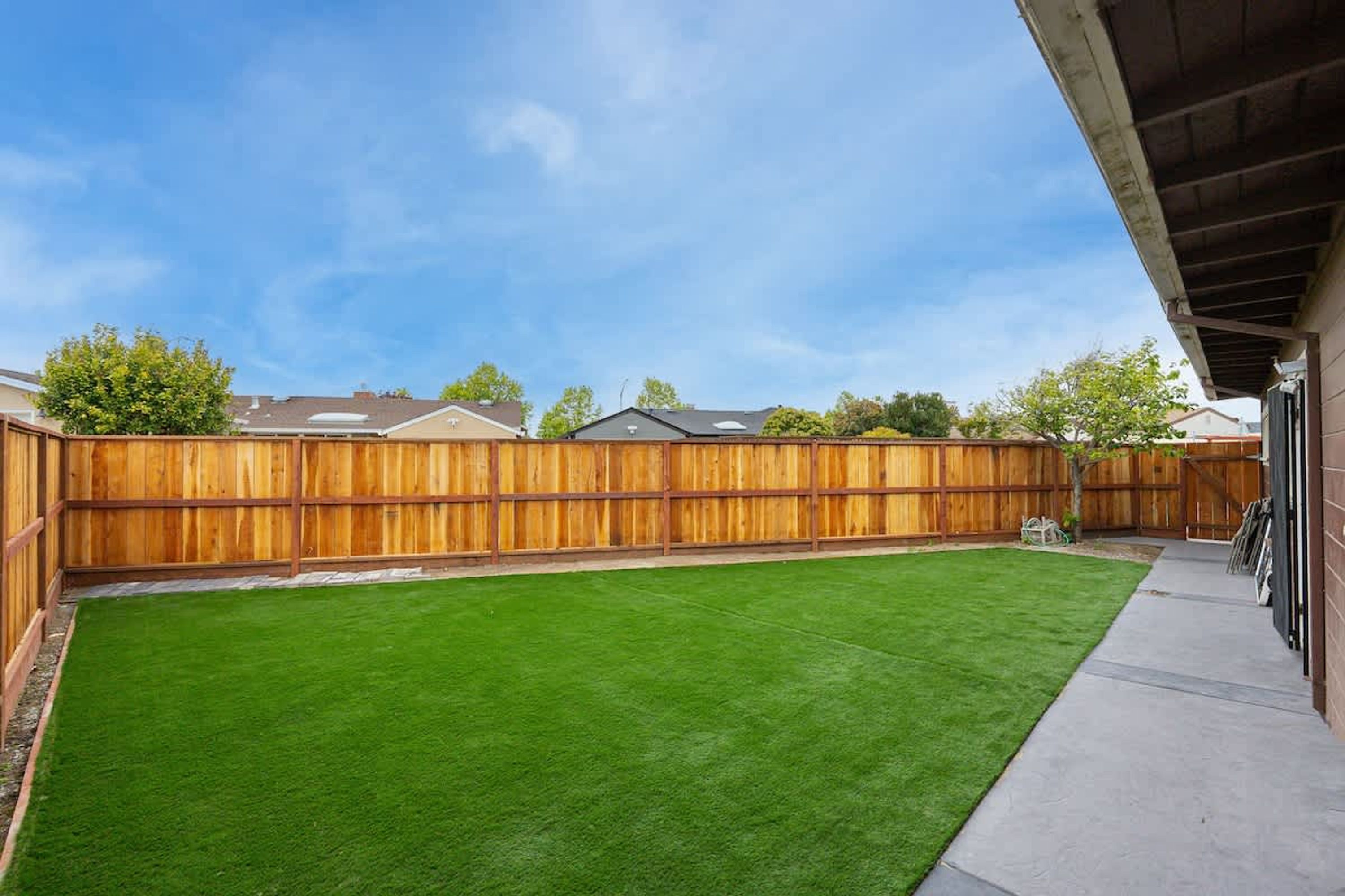 Un jardin avec une clôture en bois, une pelouse bien entretenue et un chemin en béton menant à un bâtiment.