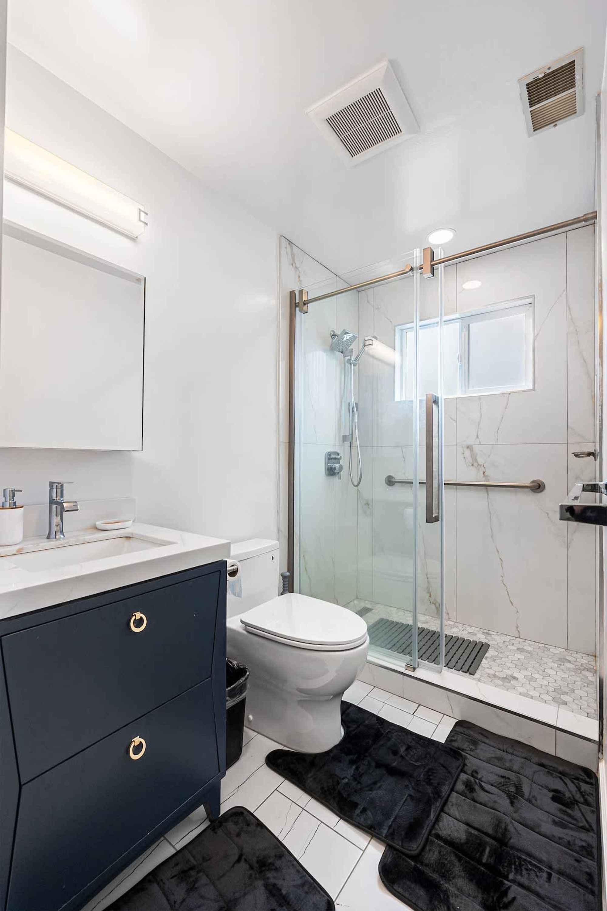 A modern bathroom with a glass-enclosed shower, a white toilet, and a dark blue vanity with gold handles.