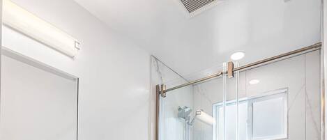 A modern bathroom with a glass-enclosed shower, a white toilet, and a dark blue vanity with gold handles.