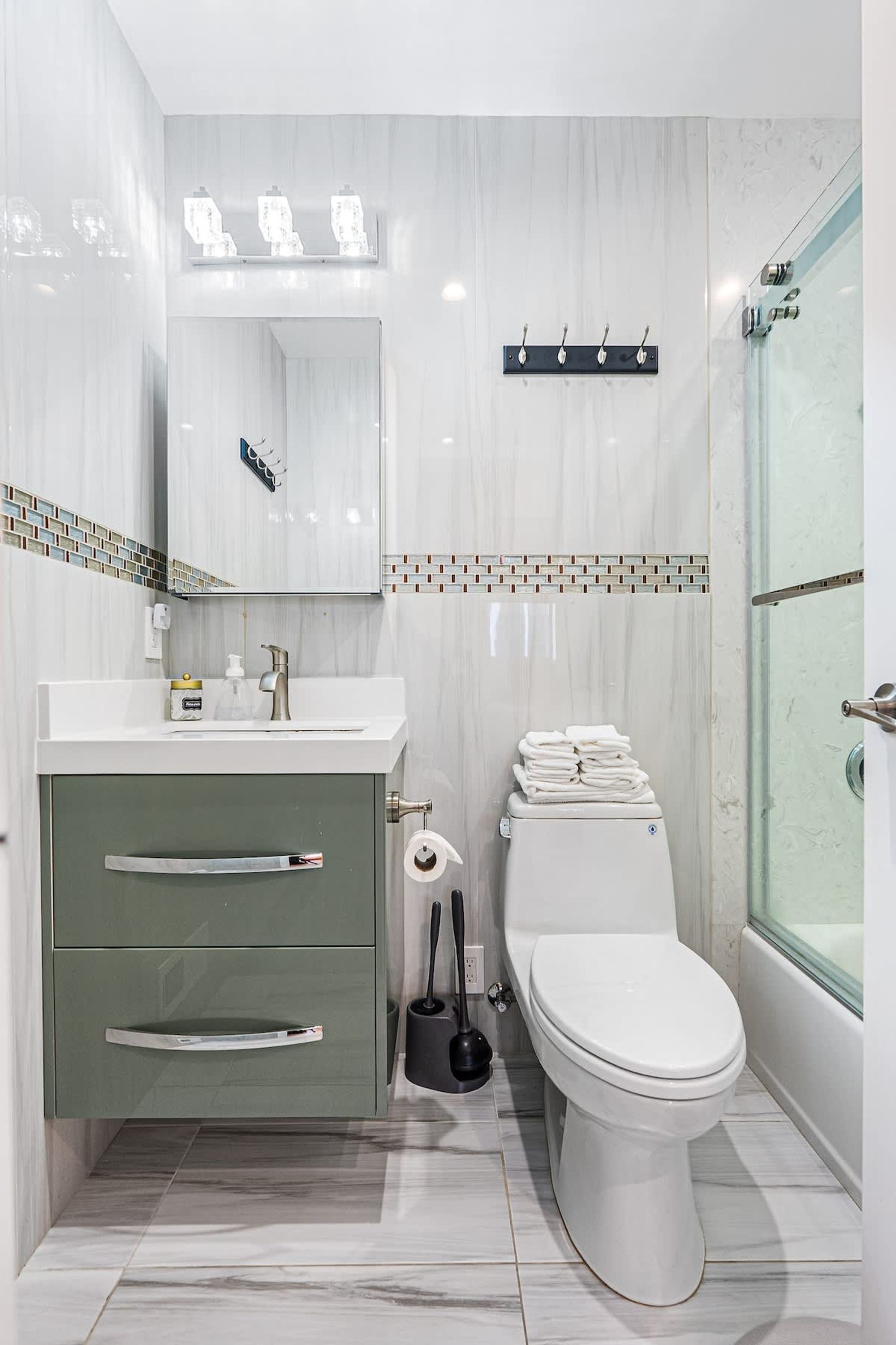 A modern bathroom with a white toilet, a green vanity, a mirror, and a shower area.