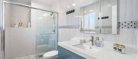 Une salle de bain moderne avec une douche à parois de verre, des toilettes blanches, un lavabo avec un meuble-vasque et un miroir au-dessus du meuble-vasque.