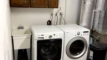 A laundry room with two washing machines, a sink, and wooden cabinets above.