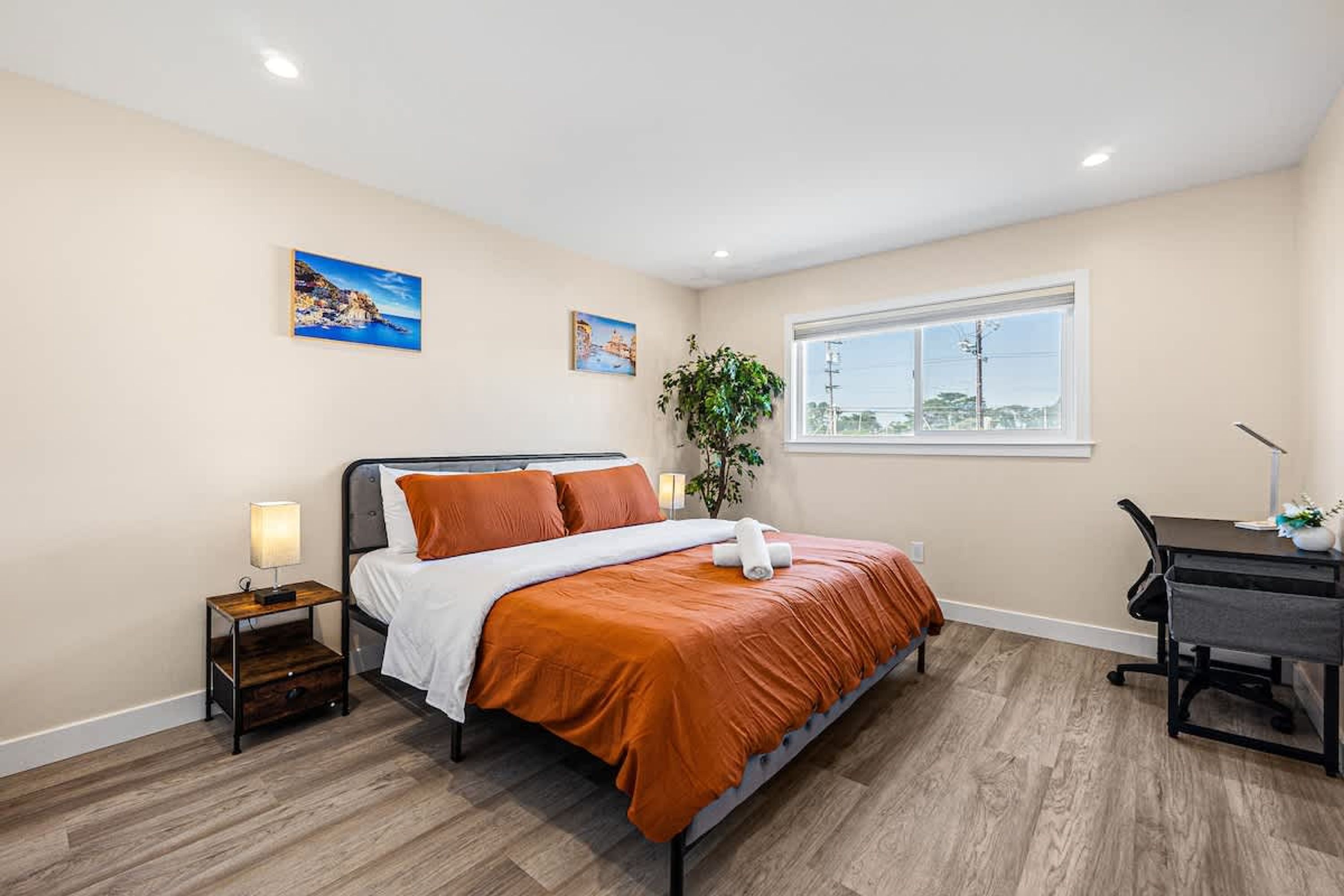 A bedroom with a bed, a desk, a nightstand, and two paintings on the wall.