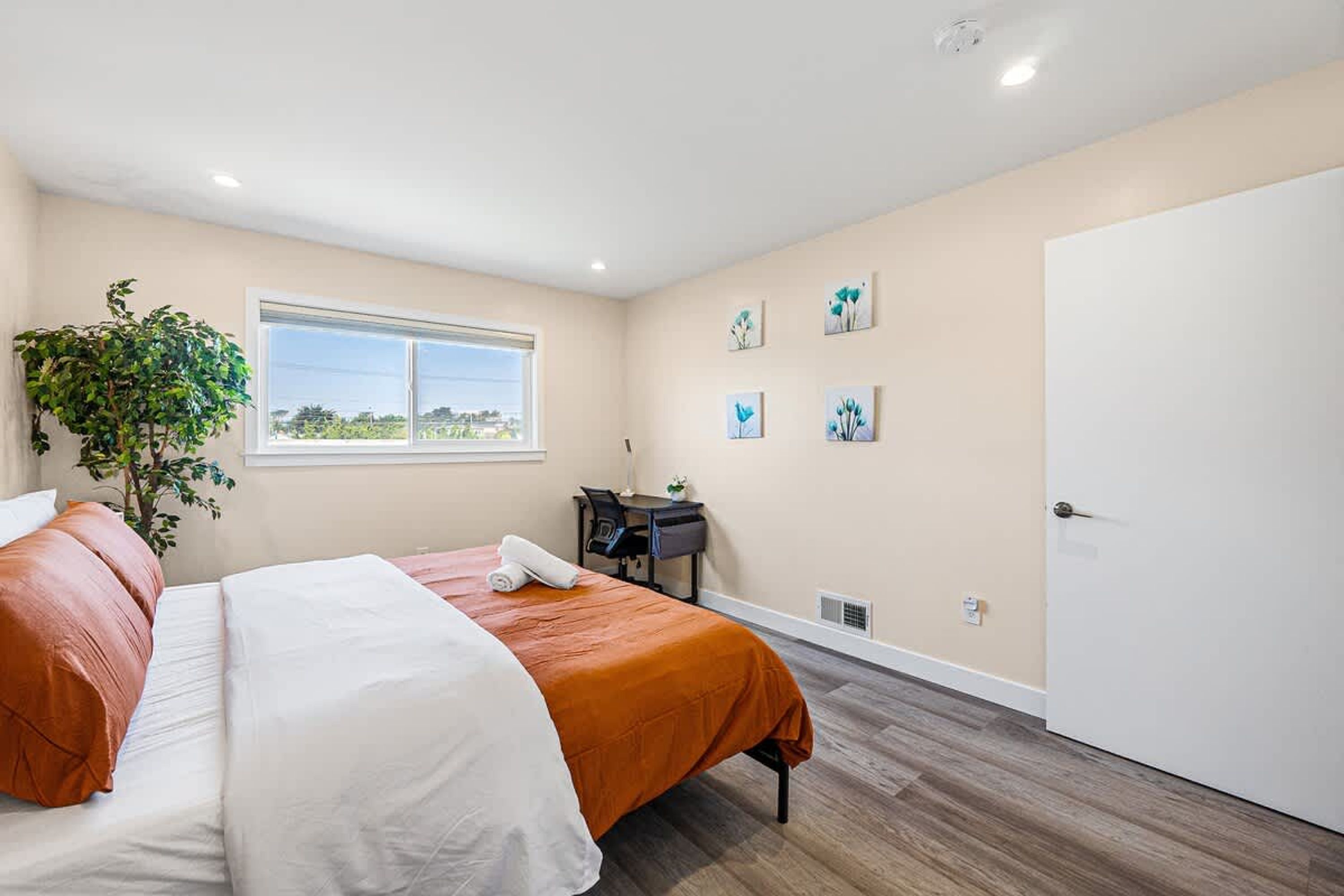 Een slaapkamer met een bed, bureau, stoel, een kamerplant en kunst aan de muur.