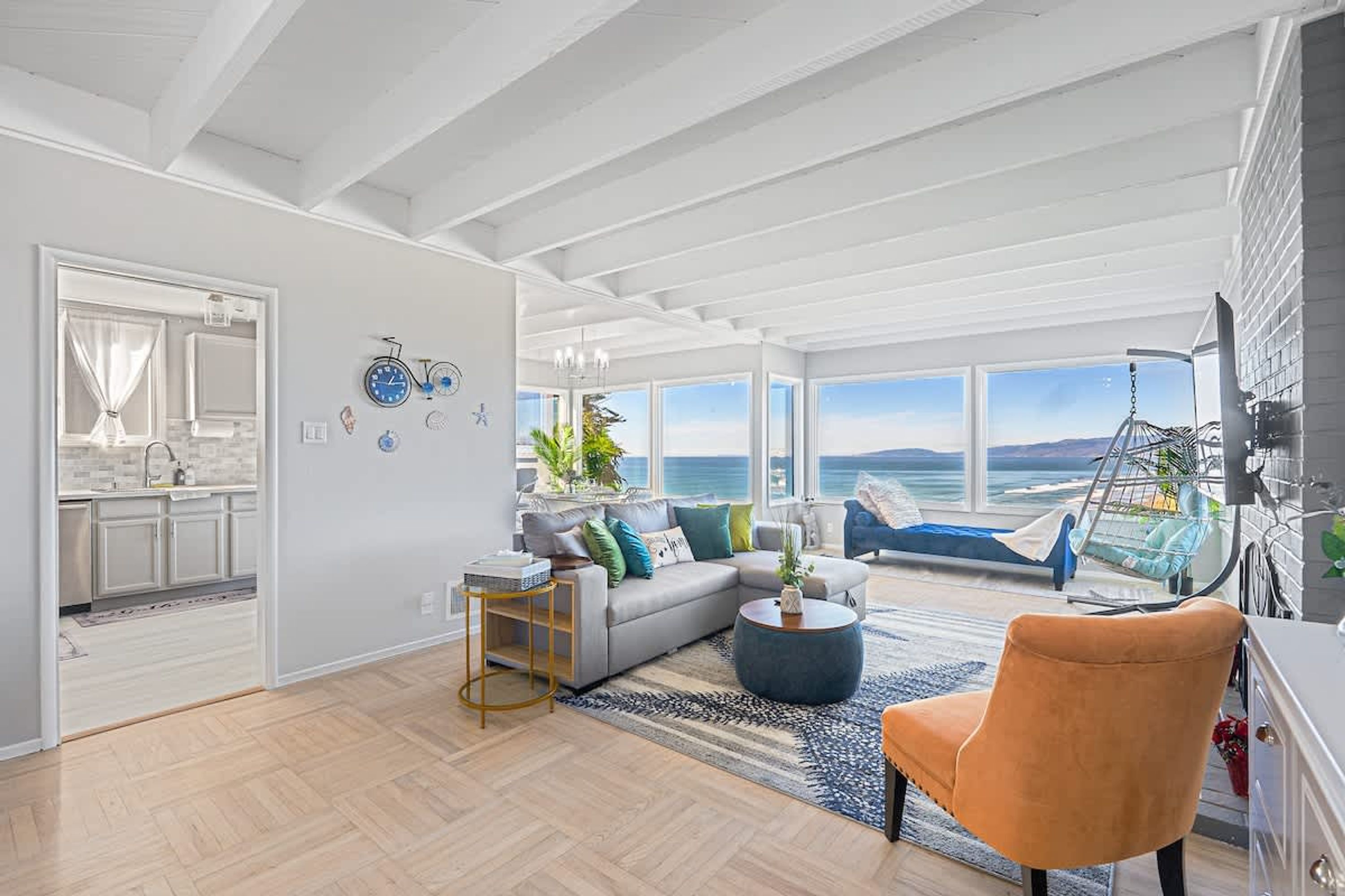 Un vaste espace de vie avec une grande fenêtre donnant sur la mer, un canapé avec des coussins, une table basse et un fauteuil.