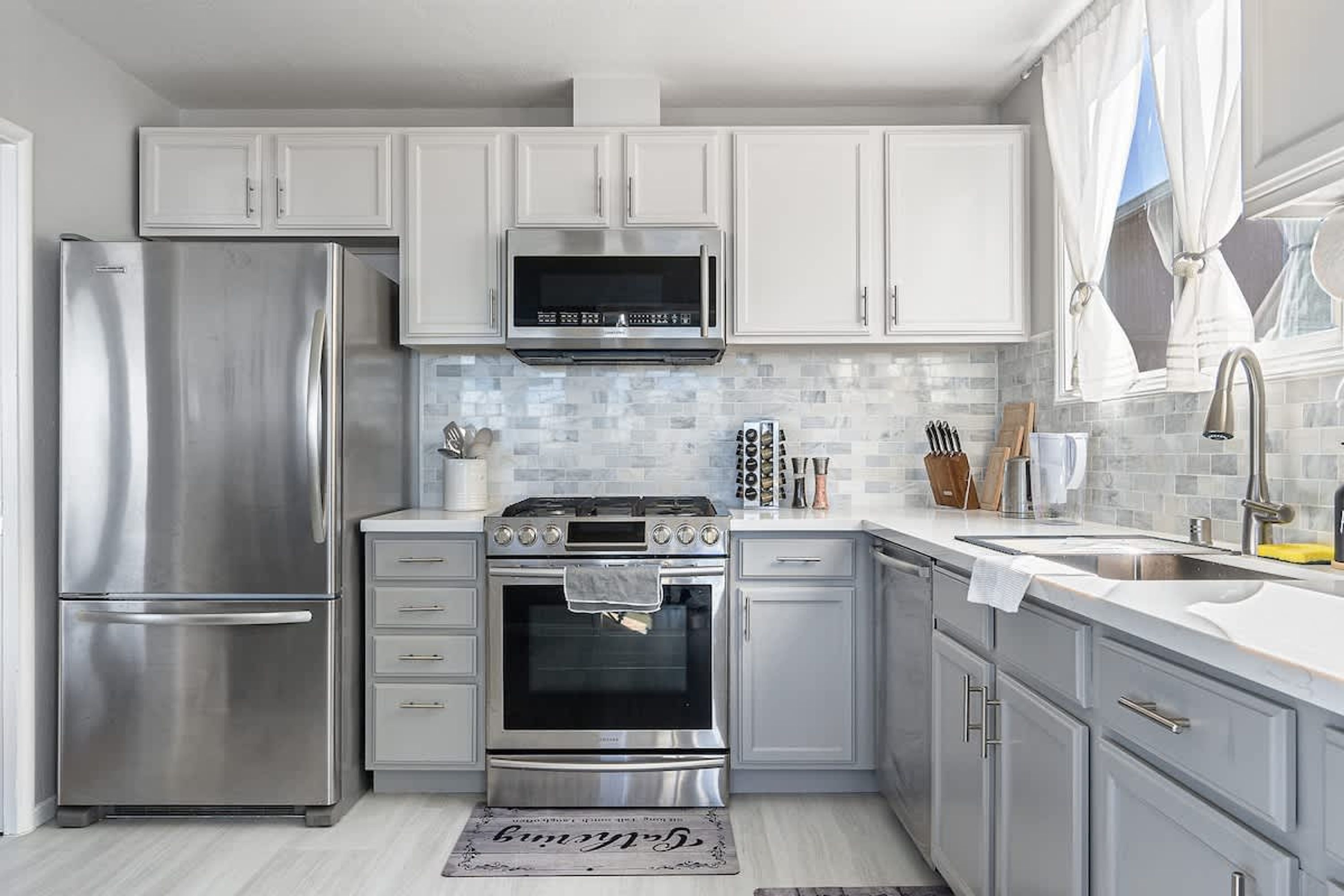 A modern kitchen with stainless steel appliances, white cabinetry, and a tiled backsplash.