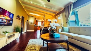 Una sala de estar moderna con ventilador de techo, televisor de pantalla plana, sofá, mesa de centro y un comedor al fondo.
