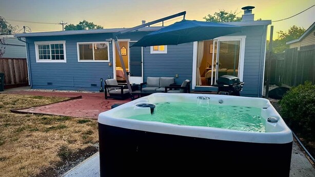 Un patio trasero con un jacuzzi, un porche cubierto y una casa con puerta corrediza.