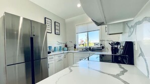 A modern kitchen with a stainless steel refrigerator, white marble countertops, and a window providing natural light. - New 3b3b Home Gogle Speed Wifi (Sunnyvale)