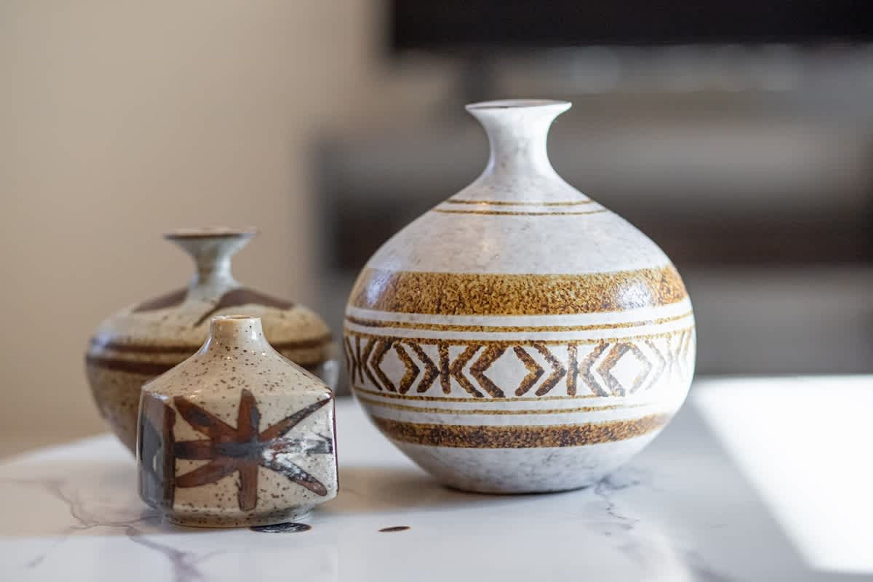Three ceramic vases with geometric patterns on a marble surface.