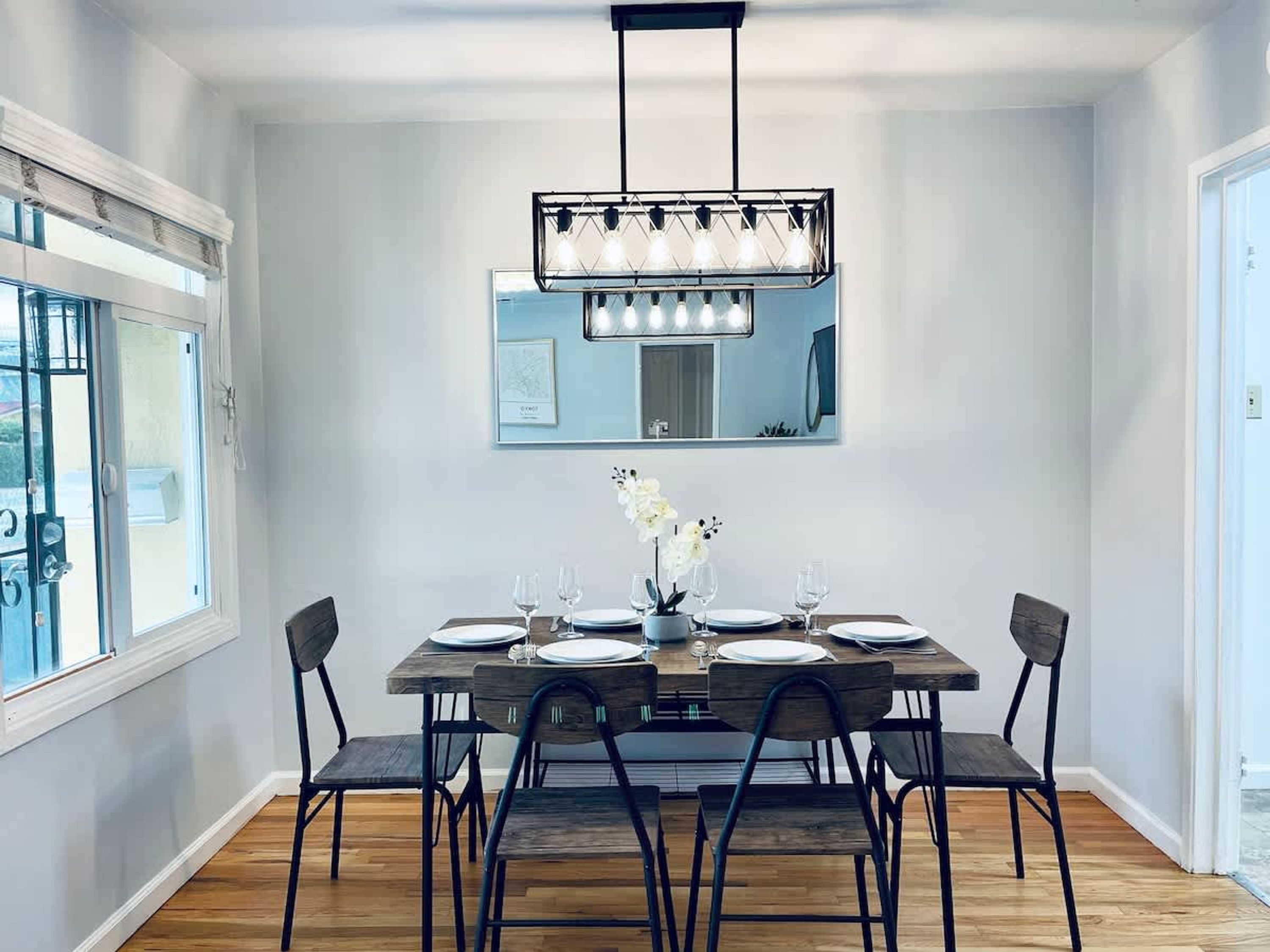 A dining area with a wooden table, six chairs, a chandelier, and a large mirror on the wall.