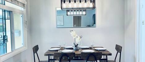 A dining area with a wooden table, six chairs, a chandelier, and a large mirror on the wall.