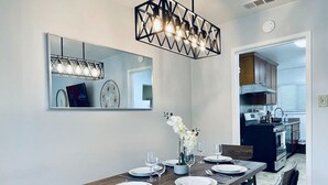 Un coin repas avec une table en bois dressée pour quatre personnes, un miroir au-dessus et une cuisine en arrière-plan.