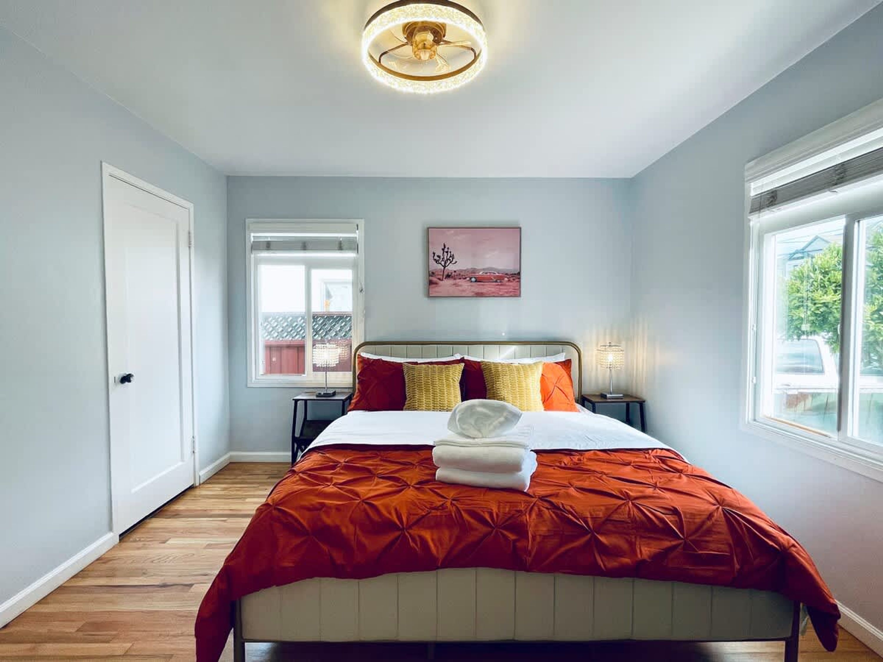 A bedroom with a bed, a nightstand, a lamp, a window, and a door.