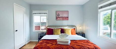 A bedroom with a bed, a nightstand, a lamp, a window, and a door.