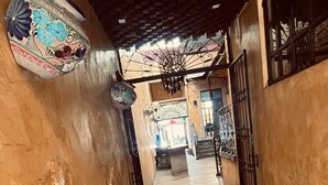 A narrow corridor with a bench and a table, a decorative ceiling, and a view into a room with a window. - Meson Acueducto (Querétaro)