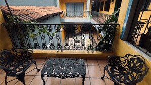 A balcony with a tiled floor, two black wrought iron chairs, a small table, and a railing with plants. - Meson Acueducto (Querétaro)