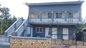 A two-story house with a stone foundation, a balcony with white railings, and a black wrought iron gate. - Cozy air conditioned 2-bedroom apartment in charming Charles Town community. (Charles town)