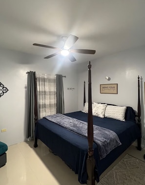 A bedroom with a four-poster bed, a ceiling fan, a wall-mounted light, and a motivational quote.