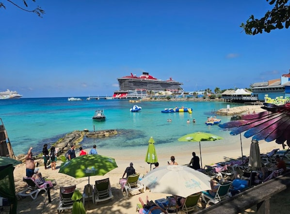 A beach with umbrellas, lounge chairs, and a cruise ship in the background.