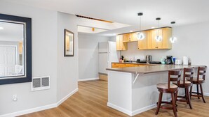 Een moderne keuken met een centraal eiland, houten kasten en barstoelen.