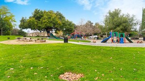 Een park met speeltoestellen, picknicktafels en een grote boom.