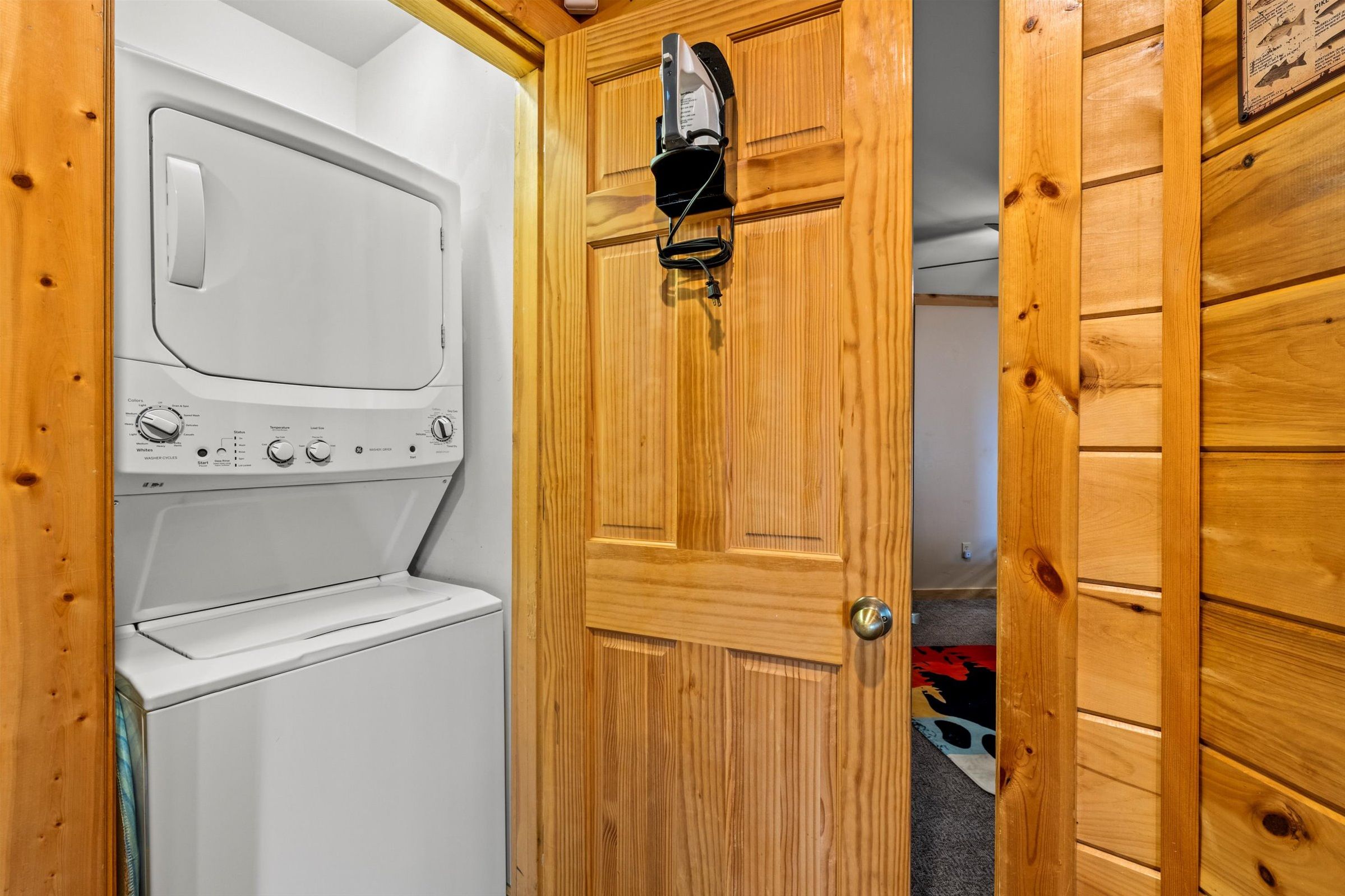 Une buanderie avec un lave-linge et un sèche-linge blancs, des murs en bois et une porte sur laquelle est accroché un fer à repasser.