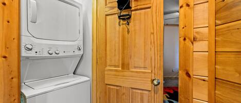 Une buanderie avec un lave-linge et un sèche-linge blancs, des murs en bois et une porte sur laquelle est accroché un fer à repasser.