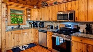 A wooden cabin kitchen with granite countertops, stainless steel appliances, and a window with blinds.