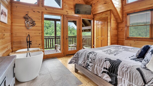 A wooden cabin with a large bed, a bathtub, and a balcony with outdoor seating. - Mountain Views, 🎯Game Room, Sleeps 20, Near Dollywood & Gatlinburg (Sevierville)