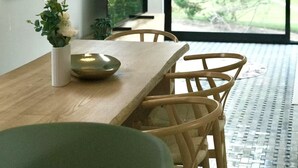 Een moderne eetruimte met een houten tafel, stoelen en een groot raam met uitzicht op groen.