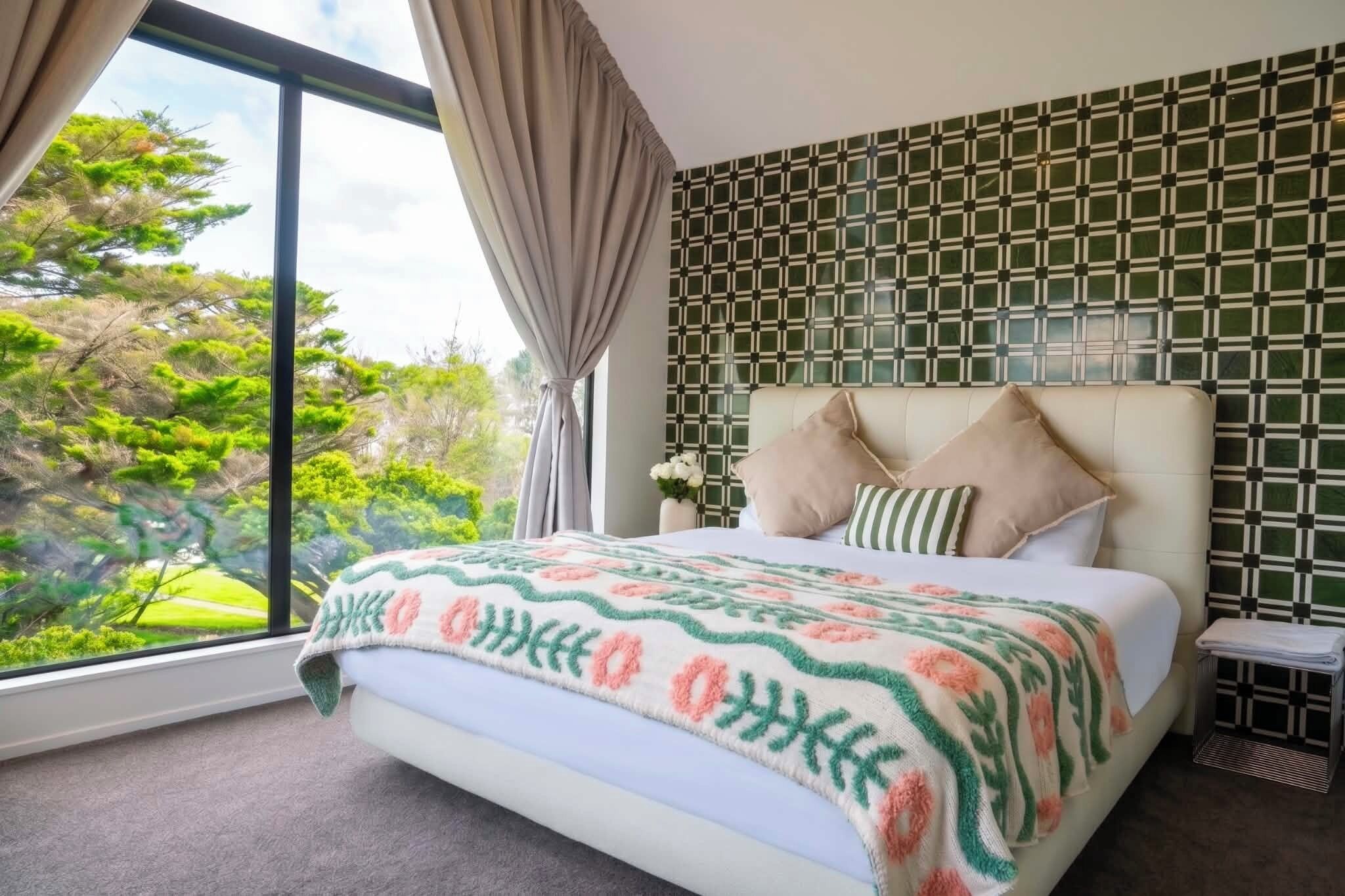 A bedroom with a large window, a bed with a patterned bedspread, and a patterned wall.