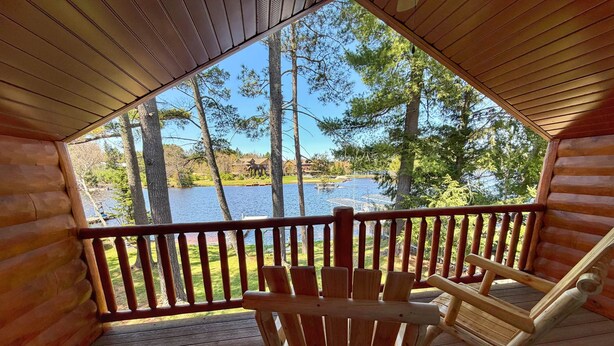 Una cabaña de madera con un porche, mecedoras y vista a un lago y árboles.