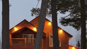 Una cabaña de madera con balcón, un porche cubierto y un terreno cubierto de nieve.