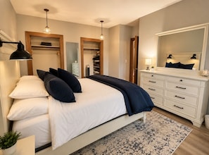 Un dormitorio con cama, lámparas de noche, cómoda, espejo y armario.