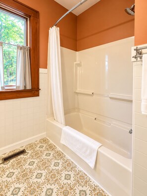 Ein Badezimmer mit Badewanne, Dusche und einem Fenster mit Vorhängen.