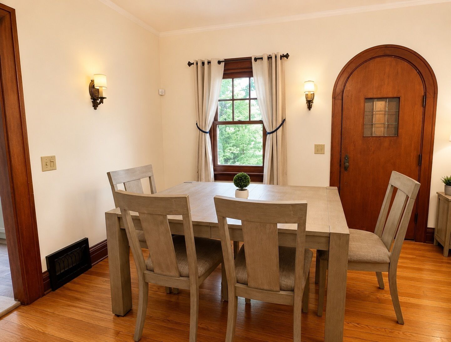 Uma sala de jantar com uma mesa e cadeiras de madeira, uma janela com cortinas e uma porta de madeira.