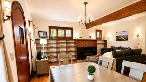 A dining area with a wooden table, chairs, a chandelier, a fireplace, and a bookshelf.